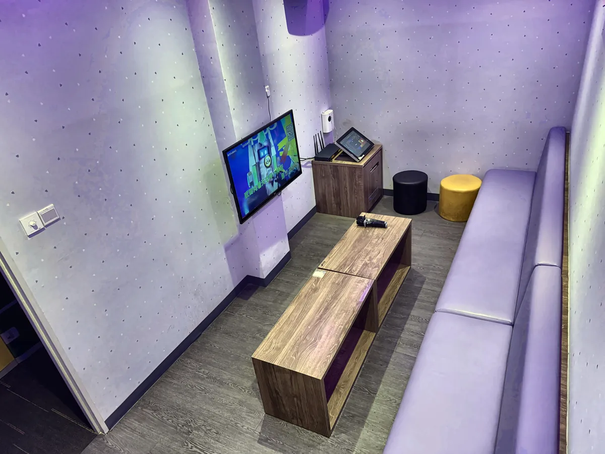 A Major 99 private karaoke room seen from above, with a wall TV, wooden coffee tables with a microphone, a purple sofa and a song-selection tablet