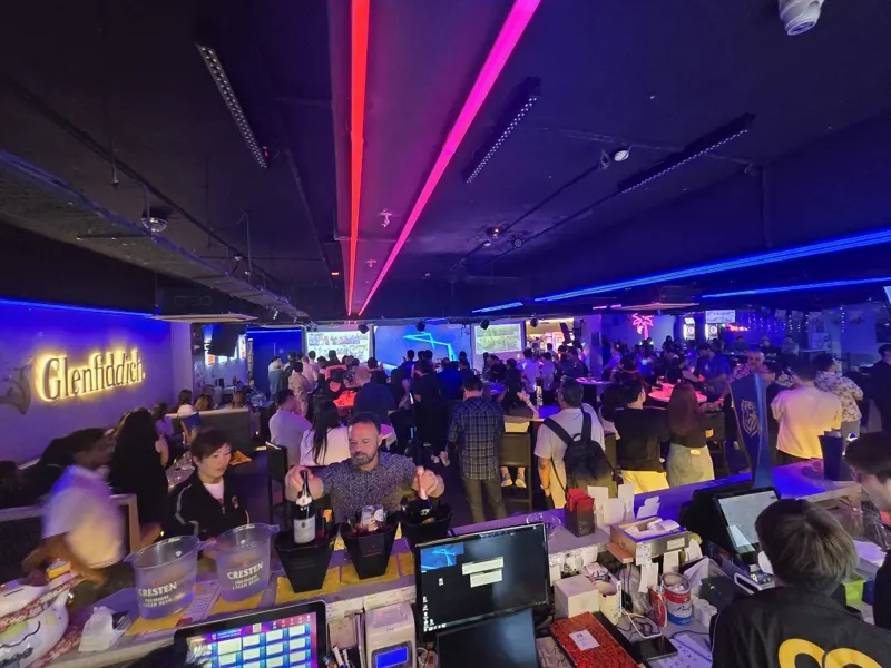 Packed floor at Major 99 seen from behind the bar, with the Glenfiddich sign and neon palm glowing