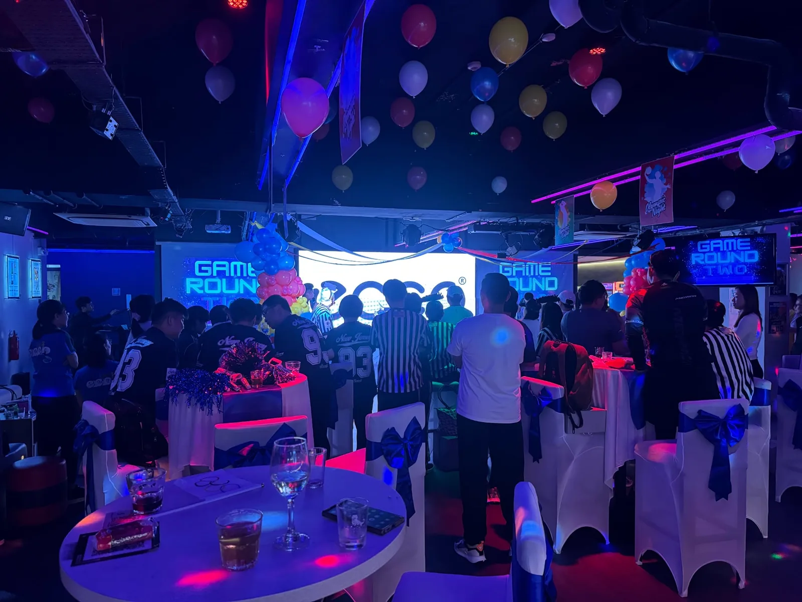 A standing crowd at a corporate games night in the Major 99 main hall, with the LED screen showing Game Round Two